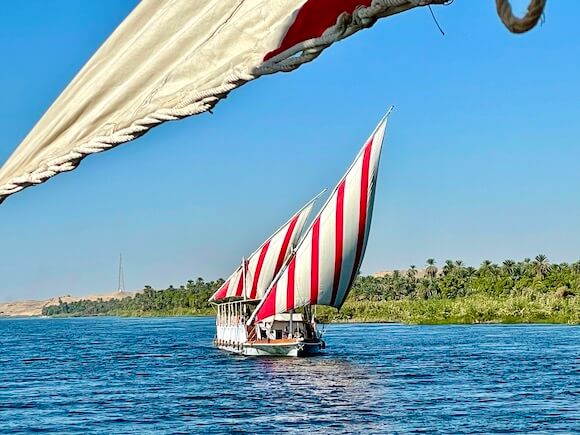 Boat with red and white sails cruising on Nile river.