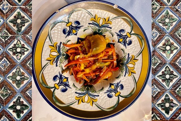 Artichoke heart on bed of vegetables on gold trimmed plate sitting on tiles