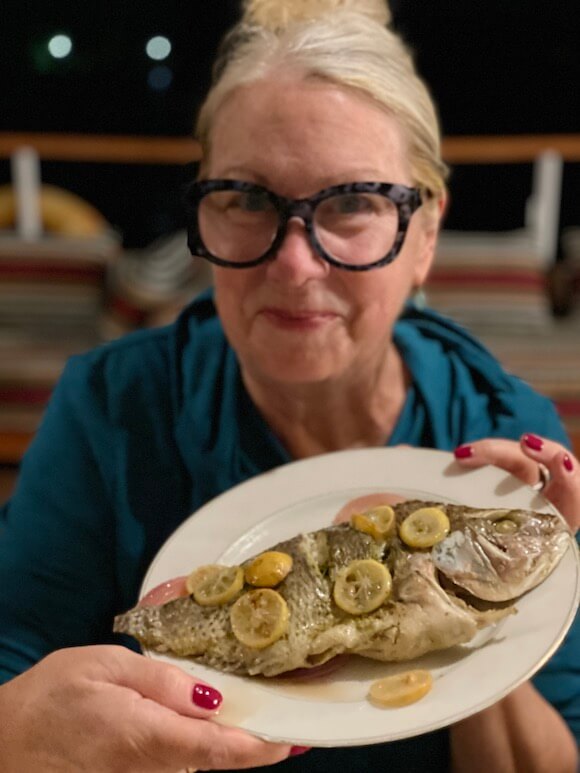 Woman with glasses holding plate of cooked fish with lemons.